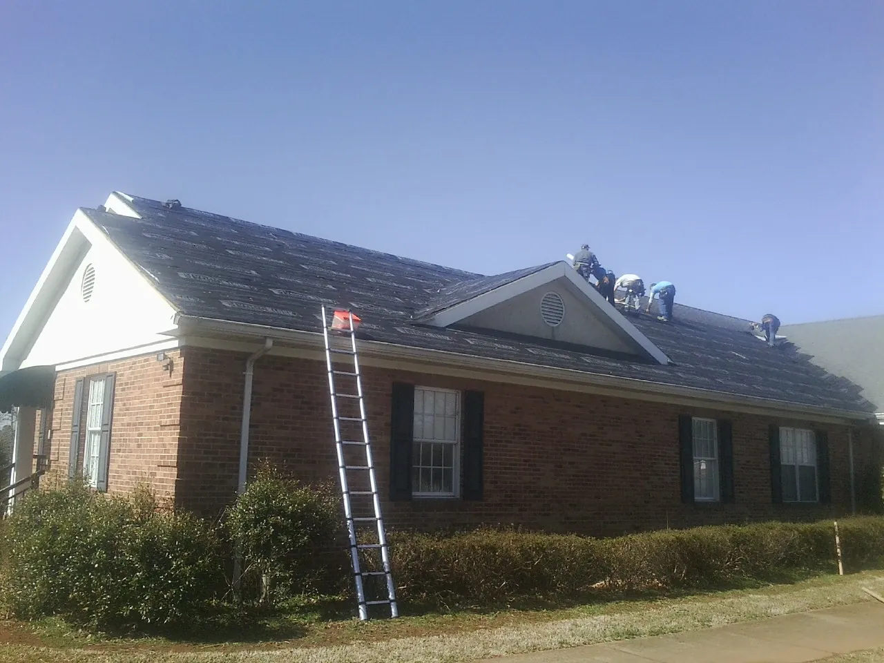 Crew tearing shingles off a brick ranch roof with a ladder set — Metal Roof Repair work by our crew in Miamisburg