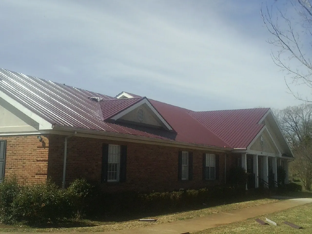 Red metal roof with gabled entries on a long brick building, from a Hail Damage Roof Repair job in Miamisburg