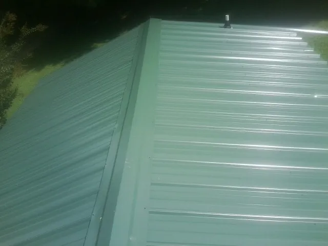 New green metal panels meeting at the ridge of a roof — Flat Roof Repair work by our crew in Miamisburg