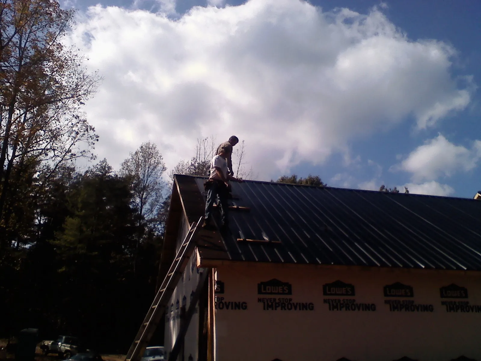 Roofer fastening dark metal panels high against a cloudy sky, from a Roof Inspection job in Miamisburg