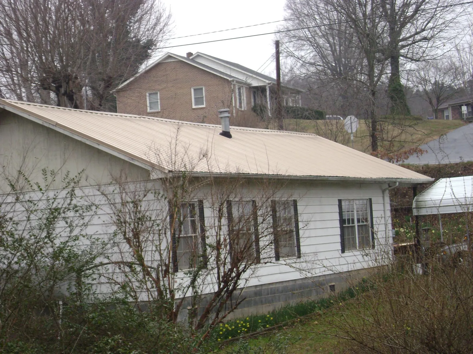 Tan metal roof on a white sided house set into a hillside — Commercial Roofing by Roofing Brothers in Miamisburg